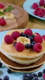 Sweet honey pouring over pancakes. Tasty breakfast food. Pancakes are served with raspberries, banana and mint leaf. Honey dripping down on dessert. Close-up, vertical footage