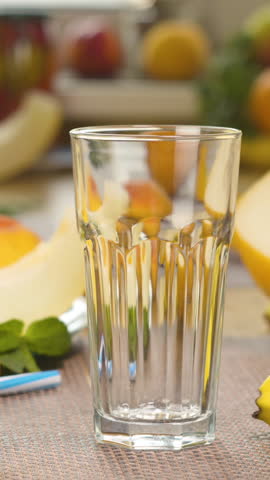 Melon banana Smoothie is poured into a glass on the background of fresh fruits. The fruit cocktail is ready to eat. Healthy and vegetarian food concept. Close up, vertical footage
