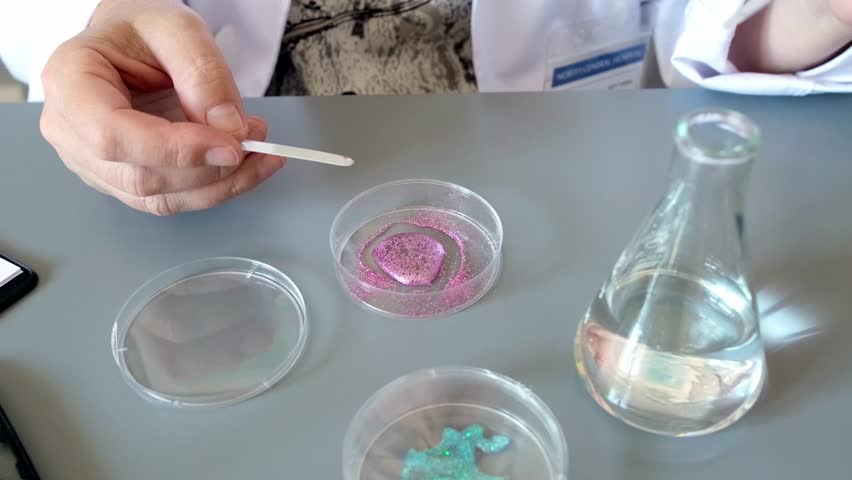 Unrecognizable female scientist pouring liquid from pipette over pink glitter sample on a petri dish in environment research lab. Woman chemist analyzing dangerous small particles on microplastics. - Powered by Shutterstock - Get 15% off with code: PIKWIZARD15