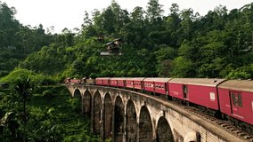 Sunrise illuminates Sri Lankan train crossing iconic Nine Arch Bridge surrounded by lush greenery. Red carriages glide over historic viaduct in hill country, Ella, scenic route for travelers. - Powered by Shutterstock - Get 15% off with code: PIKWIZARD15