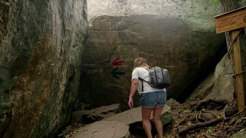 Elderly asian woman with backpack treks through narrow path in Rocky Mountains. Experienced hiker explores, enjoys solitude, mountain air. Adventurous senior challenging trail. Slow motion.