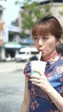 A vertical video of a Taiwanese woman in her 20s wearing a blue traditional Chinese dress in Wanhua District, Taipei City, Taiwan, walking around the town near Longshan Temple while drinking tapioca m