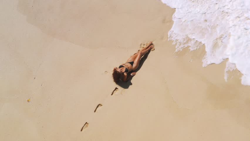 Aerial drone views a woman model in a black bikini and beautiful tropical beach with white sand and clear water. Travel and resort leisure conceptual footage with copy space