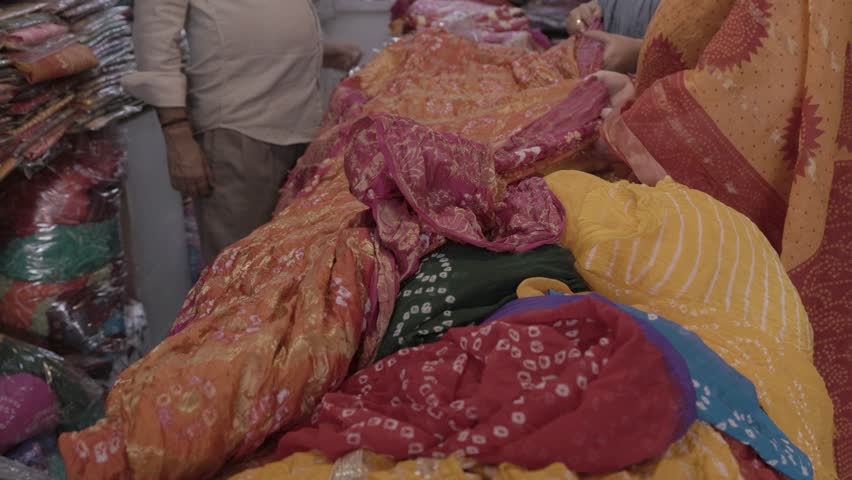 retails clothe seller showing different kind of indian traditional dress saree to customer at shop