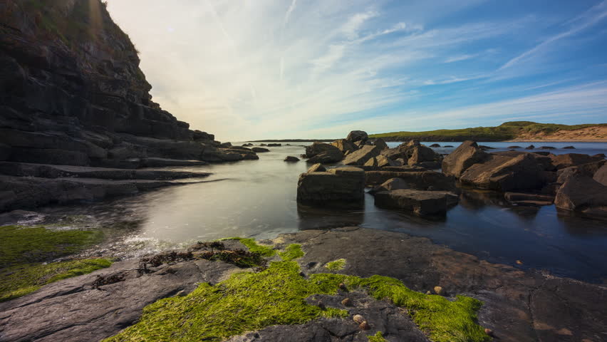 Time lapse of rising coastal tide on a sunny cloudy day on Streedagh cliff beach with sea algae and rocks in the foreground in county Sligo along Wild Atlantic Way in Ireland