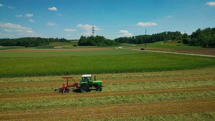 Tractor working in field in Germany. Farmer collecting cutted grass with tractor in green agriculture field. Combine harvester collects crops in spring