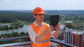 Young male builder standing on the roof while making video of construction site with digital tablet. Business, building, industry concept. Real time