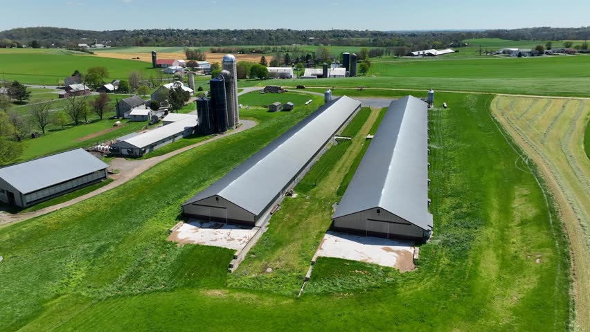 Aerial view of a large farm with long, modern barns, silos, and lush green fields in a rural landscape.