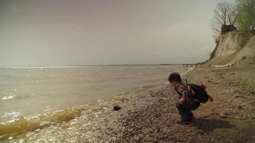 Baby boy having fun throwing stones into river. Boy throwing rocks into a river. Young Boy Throwing rocks into water.
