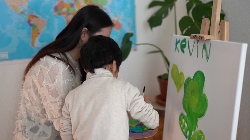 Asian teacher and little child painting on canva inside preschool class room- Mother and son doing art paint indoor - Creative activity and education concept 