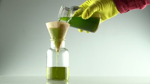 Scientist hand in yellow gloves pouring a extraction of cannabis oil and ethanol alcohol for filtration in laboratory glass bottle with filter on top filled with a mixture of liquids.