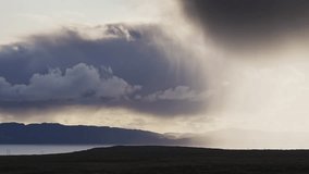 Rain falls from the dark stormy clouds backlit by the sun. Timelapse video.