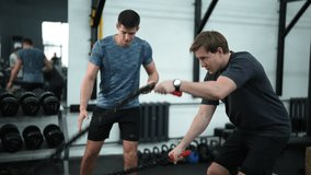 Side view of exhausted sportsman doing battle rope exercise in cross training gym with help of personal coach measuring time on stopwatch. Athletic beginner man doing battlerope exercise with coach. - Powered by Shutterstock - Get 15% off with code: PIKWIZARD15