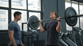 Portrait of beginner sportsman exercising at gym support under supervision of coach. Motivated athlete hard time doing barbell overhead press during weightlifting workout with help of personal trainer - Powered by Shutterstock - Get 15% off with code: PIKWIZARD15