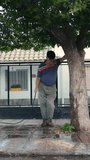 Retired man whistling while watering tree at the front of his home. Vertical video shot