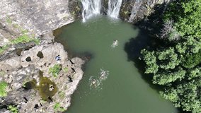 Aerial video view of a pond at Tamarind Falls, aka Seven Cascades in the tropical island jungle of Mauritius with people swimming in the pond toward the falls - with a pan up - footage 