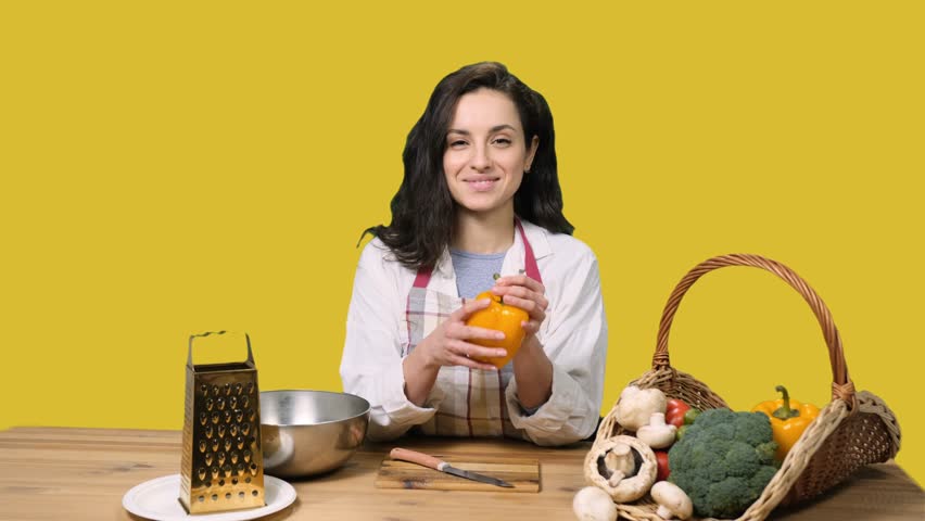 Happy young woman going to cook, holding pepper on the yellow chroma key