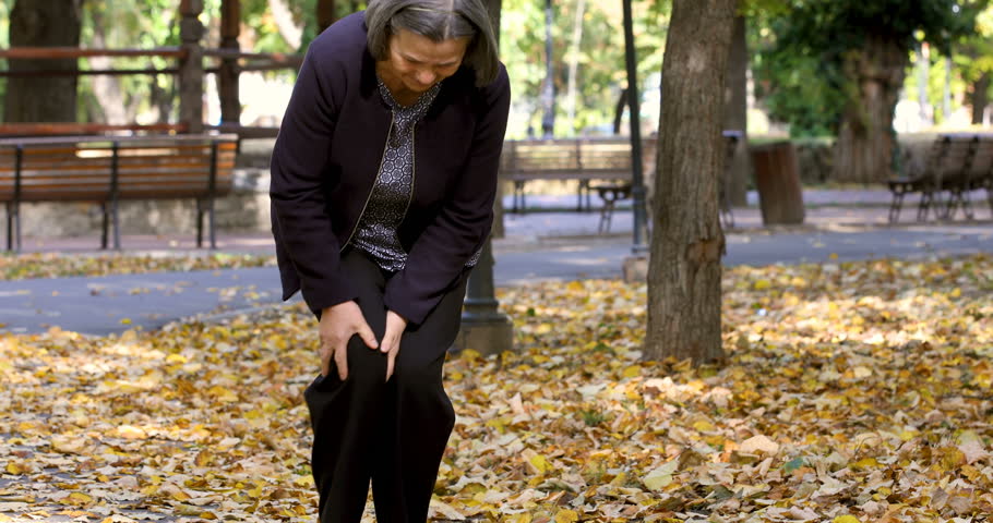 Senior woman walking in autumn park and having knee pain. Arthritis pain concept. The person comes in focus. | Shutterstock HD Video #34997359