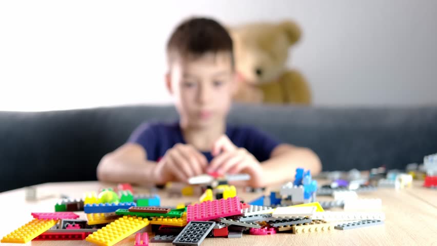 child, kid plays with colored plastic parts of the constructor, creates buildings, equipment, transport, the concept of the development of creativity, fine motor skills, patience and perseverance