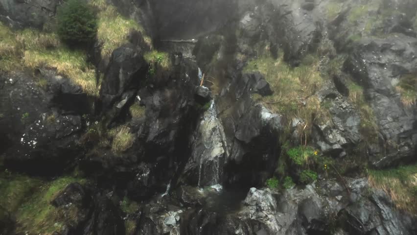 The tranquil beauty of a small waterfall cascading down a rocky and mossy rock face. Enveloped in serenity, the gentle flow of water blends the rugged texture of the rocks with some moss.