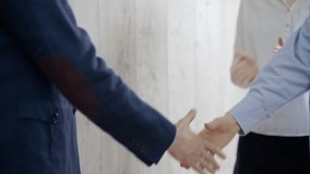 Close-up of a firm handshake between two professionals with a colleague applauding in the background