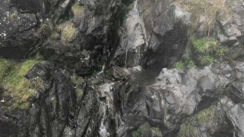 The tranquil beauty of a small waterfall cascading down a rocky and mossy rock face. Enveloped in serenity, the gentle flow of water blends the rugged texture of the rocks with some moss.