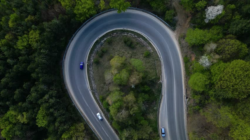 Mountain road seen from a drone. High angle fotoage of vehicles traversing a picturesque mountain curve of Shipka pass in Bulgaria. A busy European forrest road seen from above. Cars trucks driving
