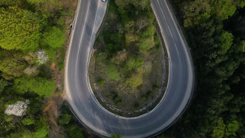 Mountain road seen from a drone. High angle fotoage of vehicles traversing a picturesque mountain curve of Shipka pass in Bulgaria. A busy European forrest road seen from above. Cars trucks driving