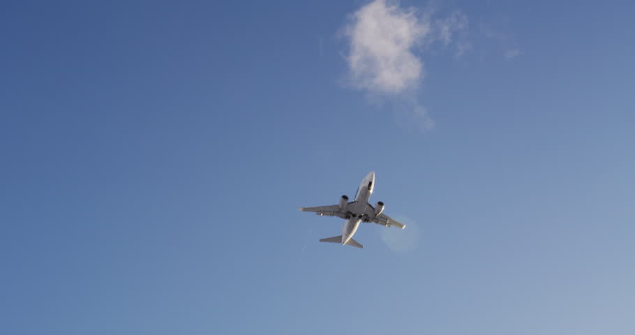 Jet plane approaching landing across blue sky, white clouds, slow-motion  