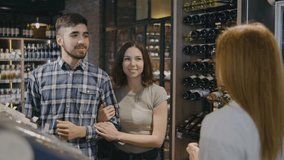 Couple in a liquor store is looking for a bottle of wine. Female worker at alcohol store gives advice to a young couple on buying alcohol. A guy and a girl walk through a liquor store and choose a - Powered by Shutterstock - Get 15% off with code: PIKWIZARD15