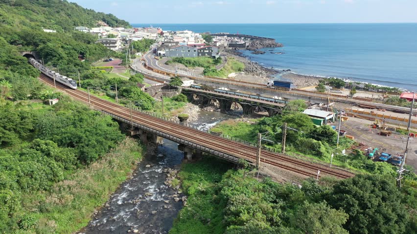 Aerial view of a Taroko Express dashing across a river by the mountainside and a coastal highway running thru a seaside village next to Daxi Harbor, in Toucheng Township, Yilan County, Taiwan