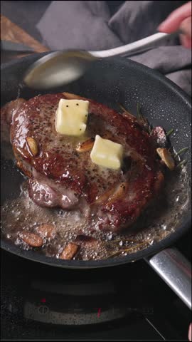 Chef pours melted butter on a juicy beef steak frying on a pan in the kitchen, food close-up. Process of cooking delicious beef steak.