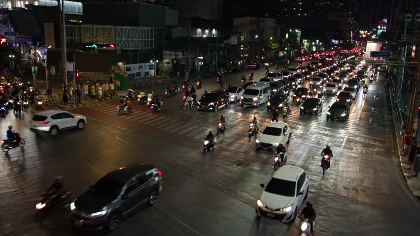 Motorcycles and cars navigate through a bustling central intersection in Bangkok, showcasing the vibrant night-time city traffic and urban life in Thailands capital.