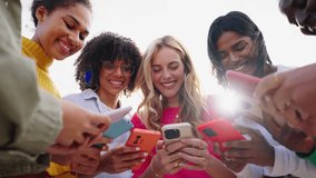 Low angle. Girls time. Group of multiracial young only women smiling gathered in circle using mobile phones. Cheerful females looking cells concentrated. Addiction to technology of gen Z - Powered by Shutterstock - Get 15% off with code: PIKWIZARD15