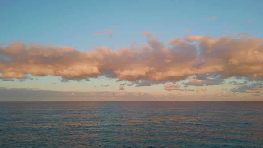 Aerial tranquil ocean sunset painting clouds pink. Peaceful horizon glowing in orange and pastel hues. Evening sky reflecting serene end of day. Reflective water mirroring seascape beauty at dusk.