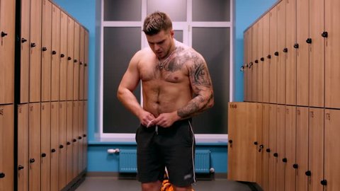 A tattooed man dresses in the gym's locker room