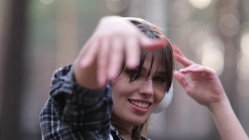 Young beautiful brunette listens to music on headphones outdoors. A woman dances joyfully to music among the maidens in the forest.