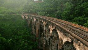 Sunrise illuminates Nine Arch Bridge, iconic Sri Lankan viaduct amid lush greenery. Early train crosses historic landmark in Ella. Travelers explore, admire colonial-era engineering in Asia. - Powered by Shutterstock - Get 15% off with code: PIKWIZARD15