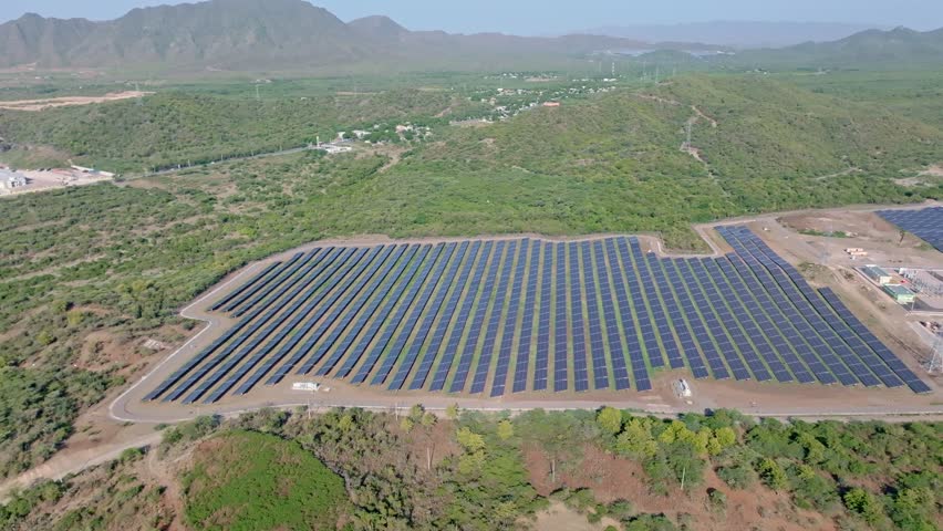 Wide aerial view of solar farm with rows of PV panels in middle of jungle