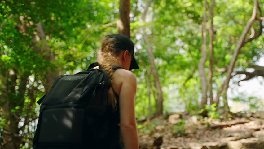 Active female hiker explores dense forest, climbs rocky terrain near scenic grotto. Backpacker on mountain trail, surrounded by natural beauty, adventure travel. Solo trekker hikes Pidurangala Rock.