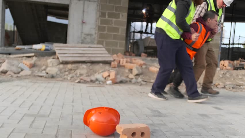 First aid team support to foreman builder worker after injury, accident at work at building site. Safety in work. Painful construction worker goes to hospital.