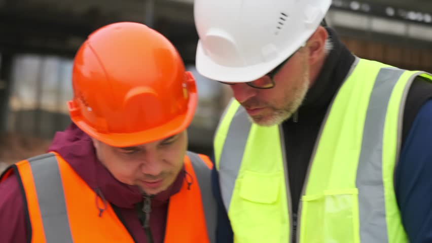 Two caucasian man foreman an contractor inspector walking arguing inspection industrial construction site, in safety hardhat and bright vests. Royalty-Free Stock Footage #3500573921
