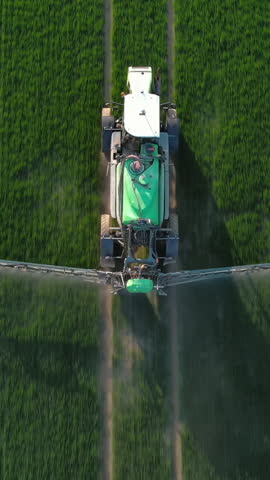 Aerial view of farming tractor crop sprayer on green field in the countryside. Vertical video