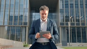 Hispanic older smiling man walking outdoor at business building using touchpad computer for work. Confident focused successful mature Indian or Latin entrepreneur businessman holding digital pc tablet - Powered by Shutterstock - Get 15% off with code: PIKWIZARD15