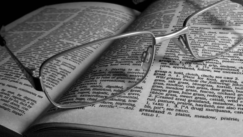 Reading glasses on a book (a dictionary), with dramatic lighting. Black and white video.