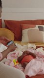 Vertical shot of young mother filming video of newborn daughter resting on bed