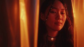 Young beautiful Asian woman with stylish hair braids standing among plastic wrap curtains and posing on camera in studio with multicolored neon light. Video portrait - Powered by Shutterstock - Get 15% off with code: PIKWIZARD15