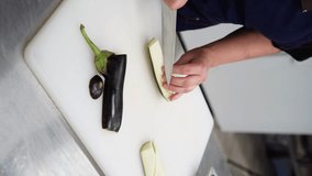 chef cuts eggplant with a knife on a white board. vertical video