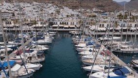 A short drone video captures sailboats docked at a harbor in Gran Canaria. The drone glides past their towering masts, showcasing the intricate details and impressive scale of the boats against the se
