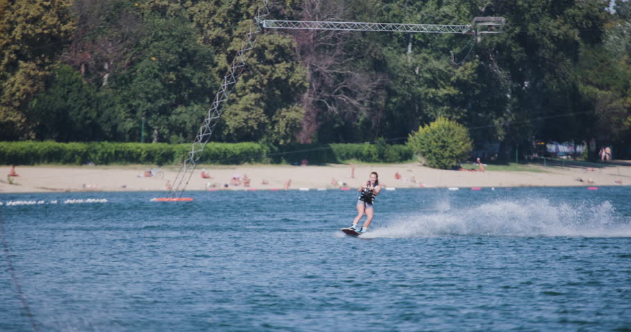 Female wakeboarder wakesurfing. Girl riding on waterski cable. Holding tow rope. Recorded at 120fps.